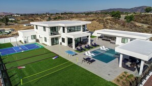 A modern two-story house with a tennis court, pool, and outdoor seating area. - Villa Fabulosa - Luxurious Bedrooms, Pool, Pickleball, Mini Golf, Game Room, 360 degree view and more (Temecula)