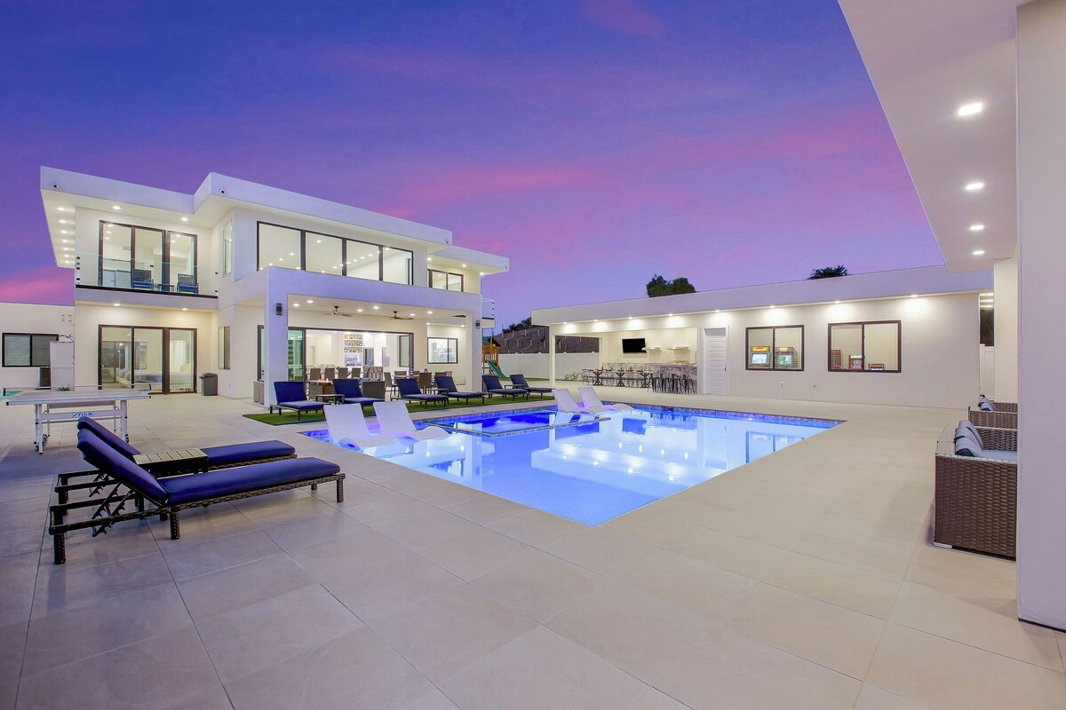Ein modernes Haus mit Swimmingpool, Sitzgelegenheiten im Freien und einer gut beleuchteten Terrassenfläche.