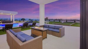 An outdoor patio with wicker furniture, a fire pit, and a view of a golf course at dusk. - Villa Fabulosa - Luxurious Bedrooms, Pool, Pickleball, Mini Golf, Game Room, 360 degree view and more (Temecula)