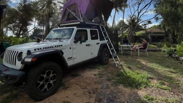 Un veicolo fuoristrada bianco parcheggiato in un ambiente naturale con una tenda sul tetto.