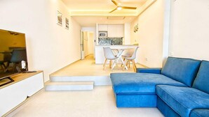 Una sala de estar moderna con un sofá azul, un televisor de pantalla plana y una zona de comedor con sillas y una mesa.