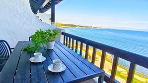 Un balcón con vista al mar, una mesa con dos tazas y una planta en maceta.