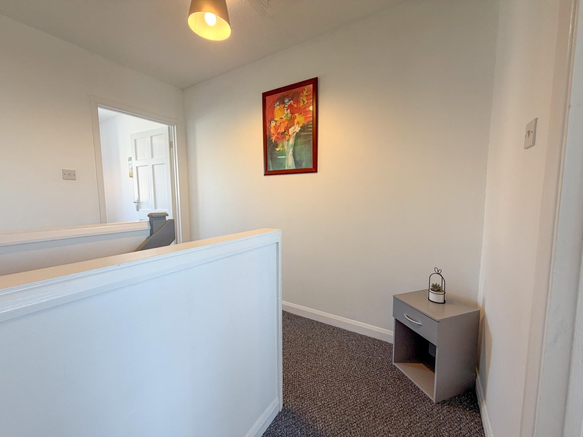 A hallway with a white partition, a small gray cabinet, a framed painting, and a door leading to another room.