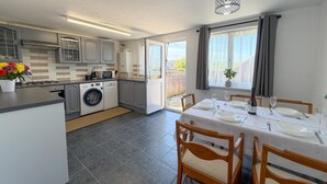 Una cucina moderna con lavatrice integrata, un'area pranzo con tavolo imbandito per quattro persone e un'ampia finestra con tende.