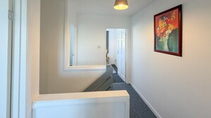 Un corridoio con una scala, un lampadario e un quadro appeso al muro.