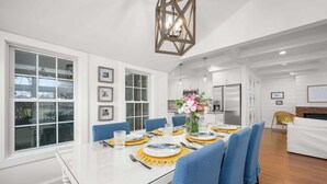 Uma sala de jantar com uma mesa branca, cadeiras azuis e um lustre.