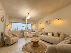 Ein geräumiger Wohnbereich mit einer Couch, Sesseln, einem Couchtisch und einer Treppe, die auf einen Balkon führt.