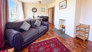 A living room with a sofa, a dining table, a piano, and a fireplace. - Indigo Blue - 2 Bedroom Holiday Home - Manorbier (Tenby)