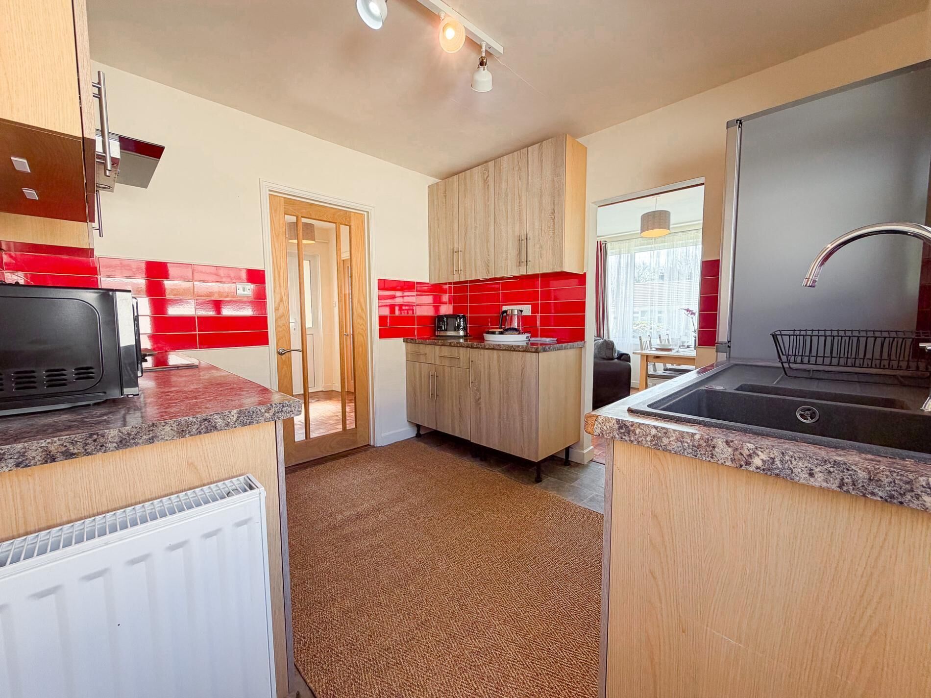 A compact kitchen with a microwave, a sink, and a door leading to another room.
