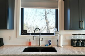 A kitchen with a window, a sink, a faucet, a soap dispenser, a paper towel holder, and a coffee maker.