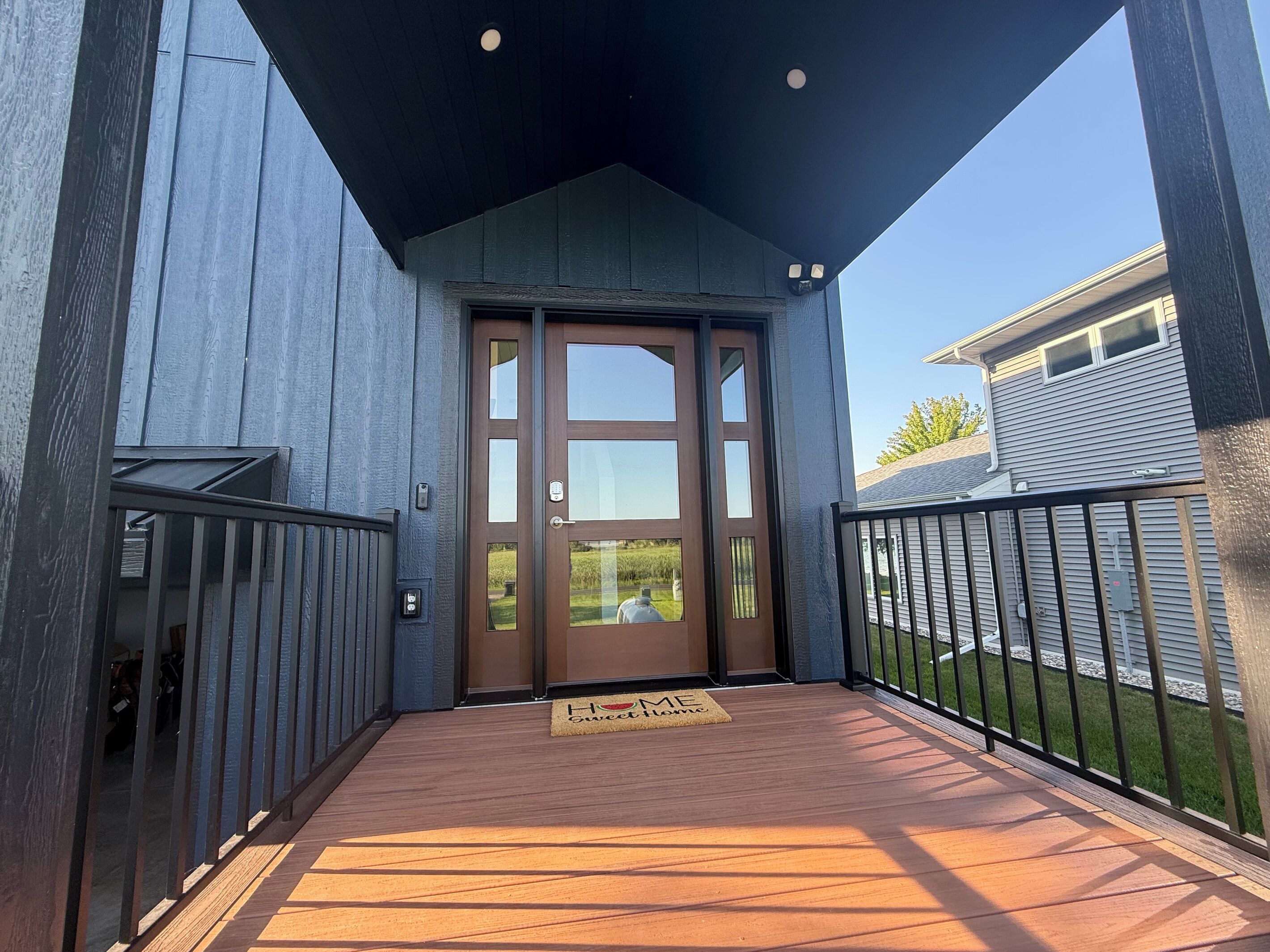 Eine überdachte Veranda mit Holzboden, eine braune Tür mit Glasfeldern und ein Metallgeländer.