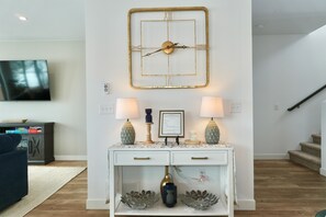 A living room with a mounted clock, two lamps, a framed picture, and a television on the wall.