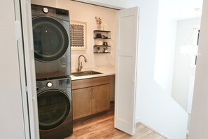 A compact kitchen with a double washer, a sink, wooden cabinets, and a chalkboard with laundry tips. - Lakeside Luxe on Pickerel (Richville)