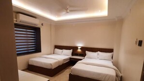 A compact hotel room with two beds, a small desk, a window with blinds, and a ceiling fan. - Airavat (Bhubaneshwar)