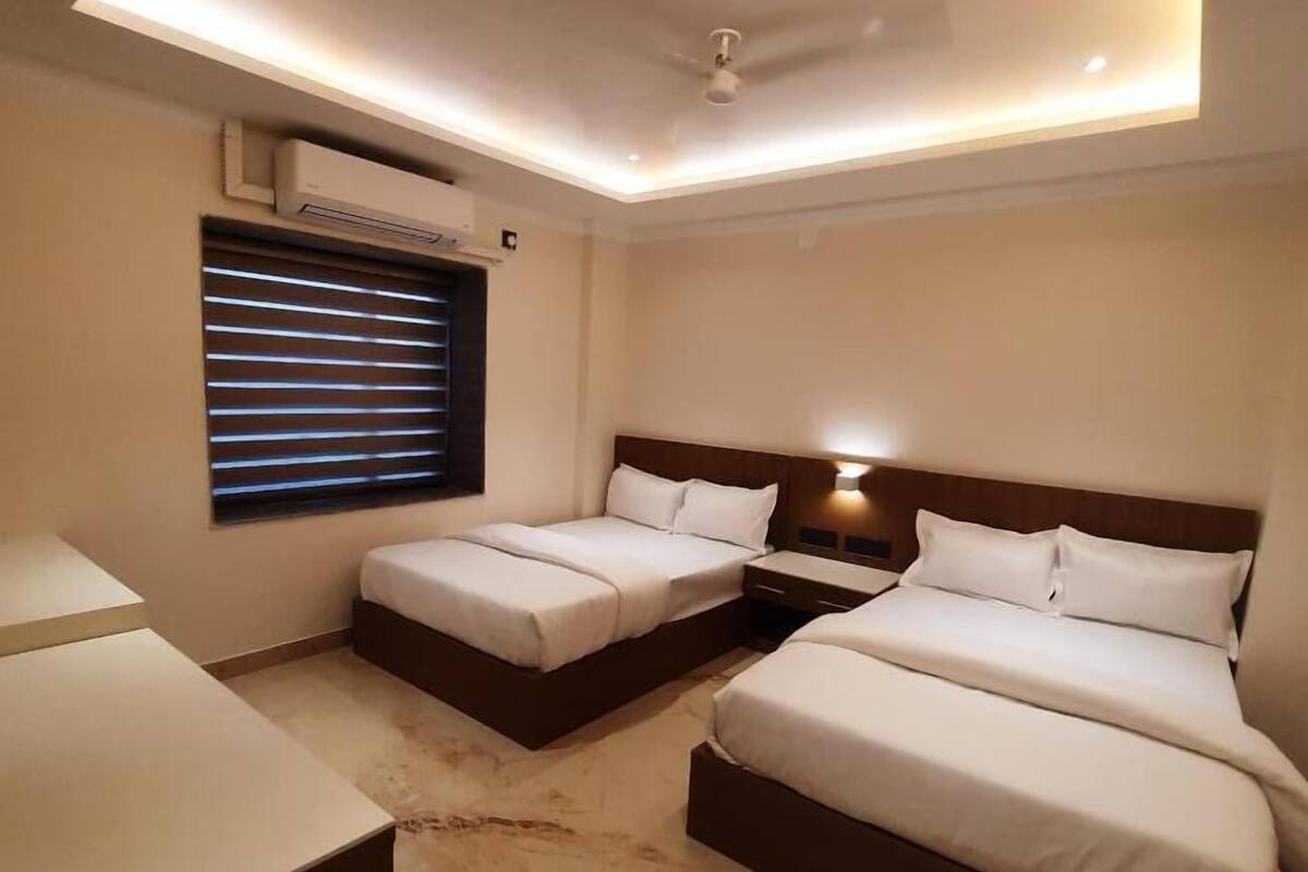 Habitación de hotel con dos camas, un escritorio, una ventana con persianas, un equipo de aire acondicionado y un ventilador de techo.