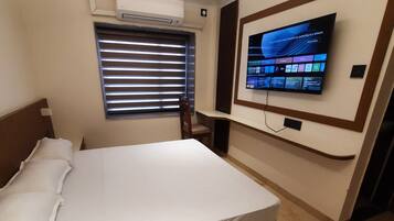 Habitación de hotel con cama, televisión montada en la pared, ventana con persianas y aire acondicionado.
