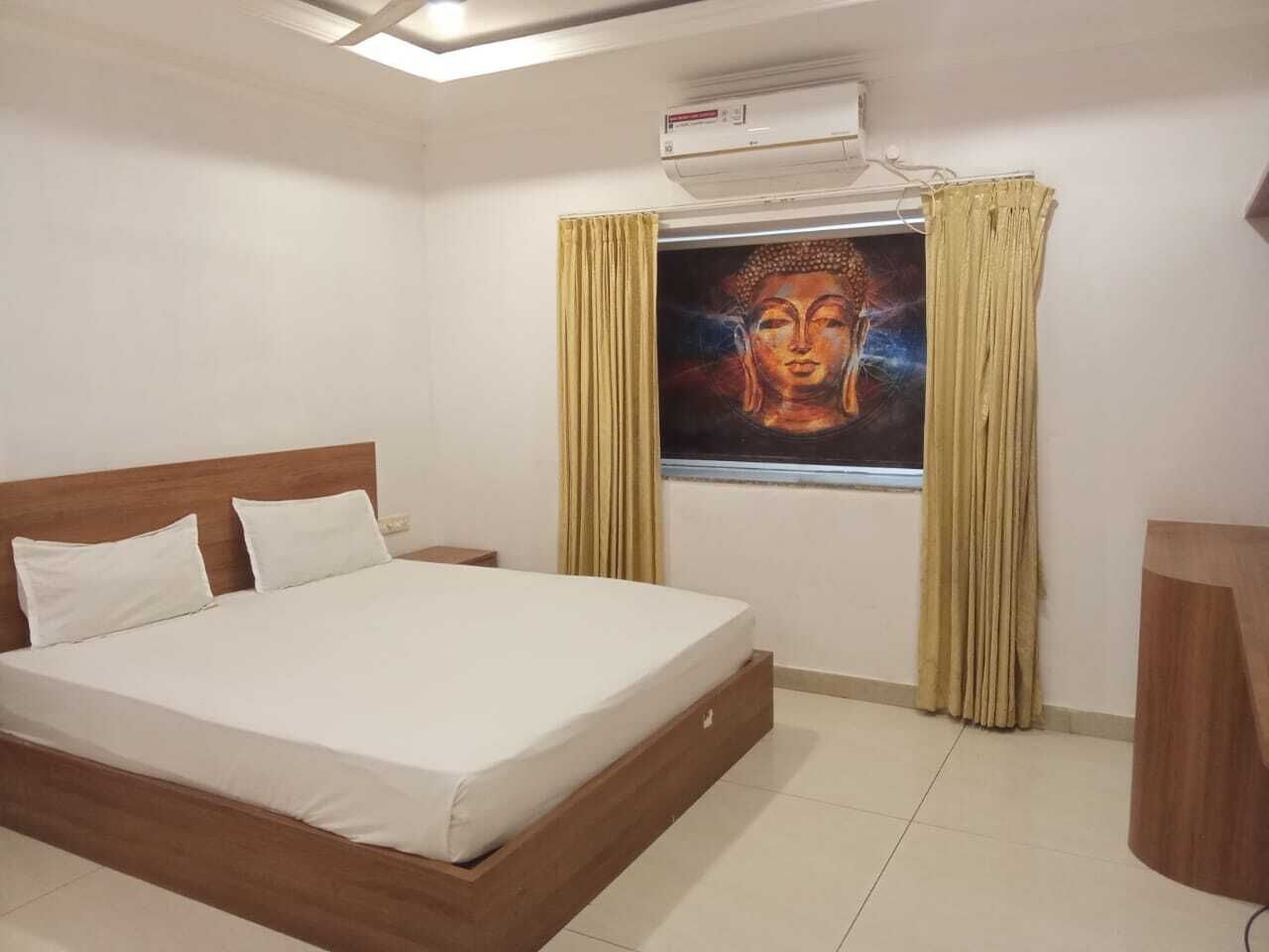 Habitación de hotel con cama, cortinas, un cuadro, equipo de aire acondicionado y cabecero de madera.