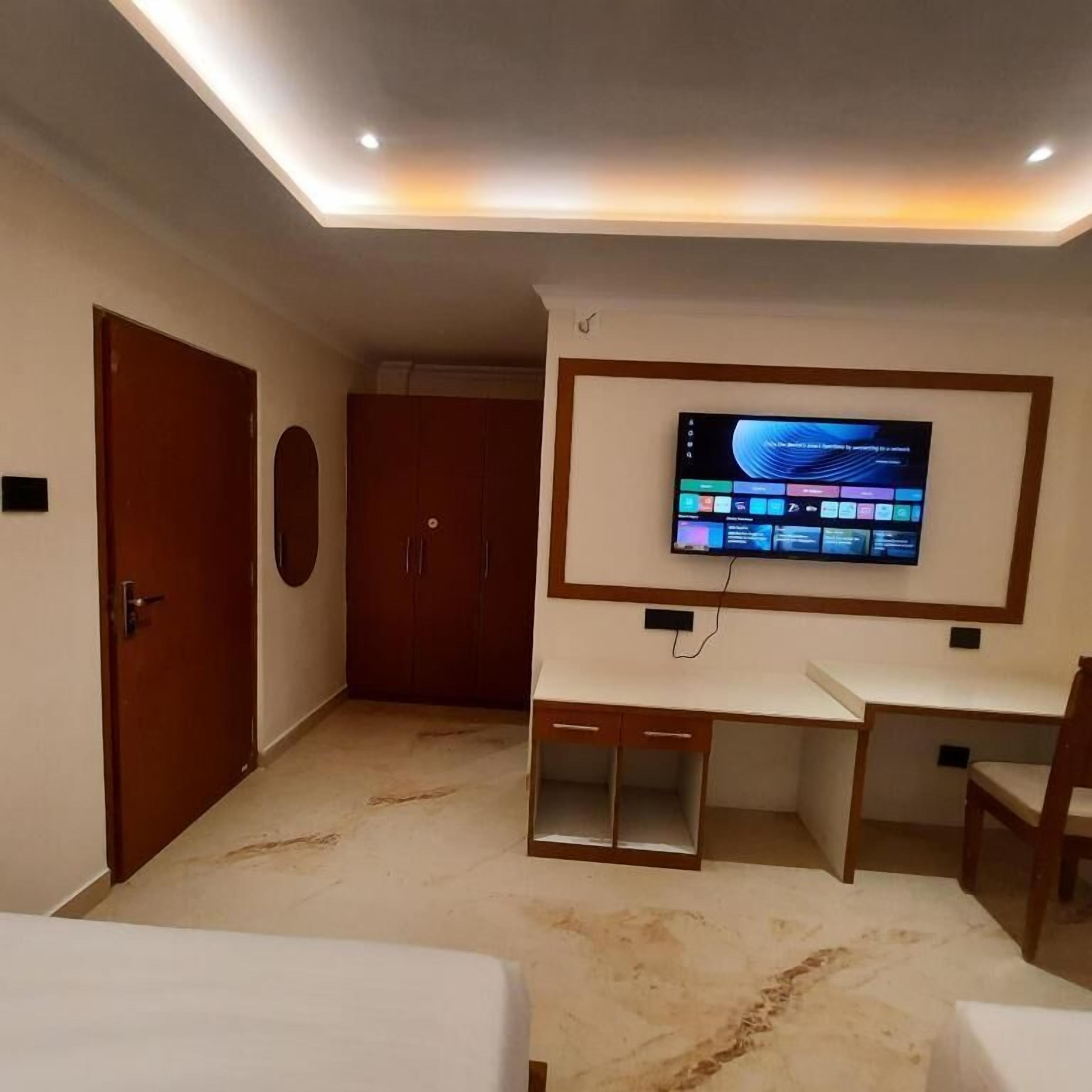Habitación de hotel con una televisión montada en la pared, un escritorio, un armario y una cama.