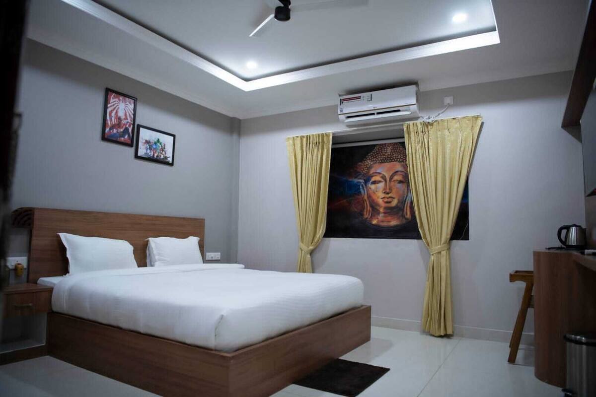Una habitación de hotel moderna con una cama de madera, un equipo de aire acondicionado, un ventilador de techo y un cuadro de Buda.