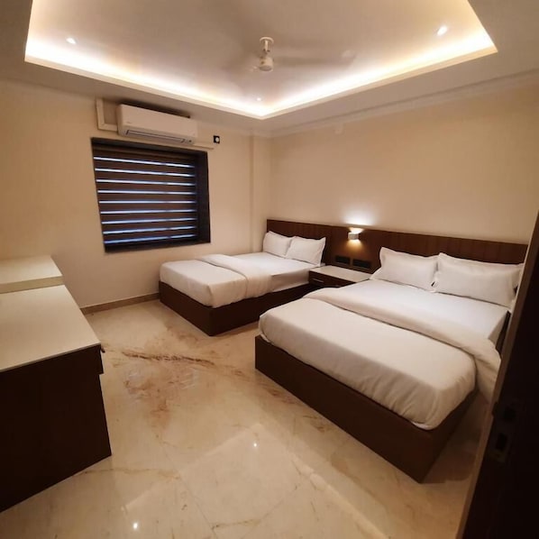 A hotel room with two beds, a desk, a window with blinds, an air conditioning unit, and a ceiling light. - Airavat (Bhubaneshwar)
