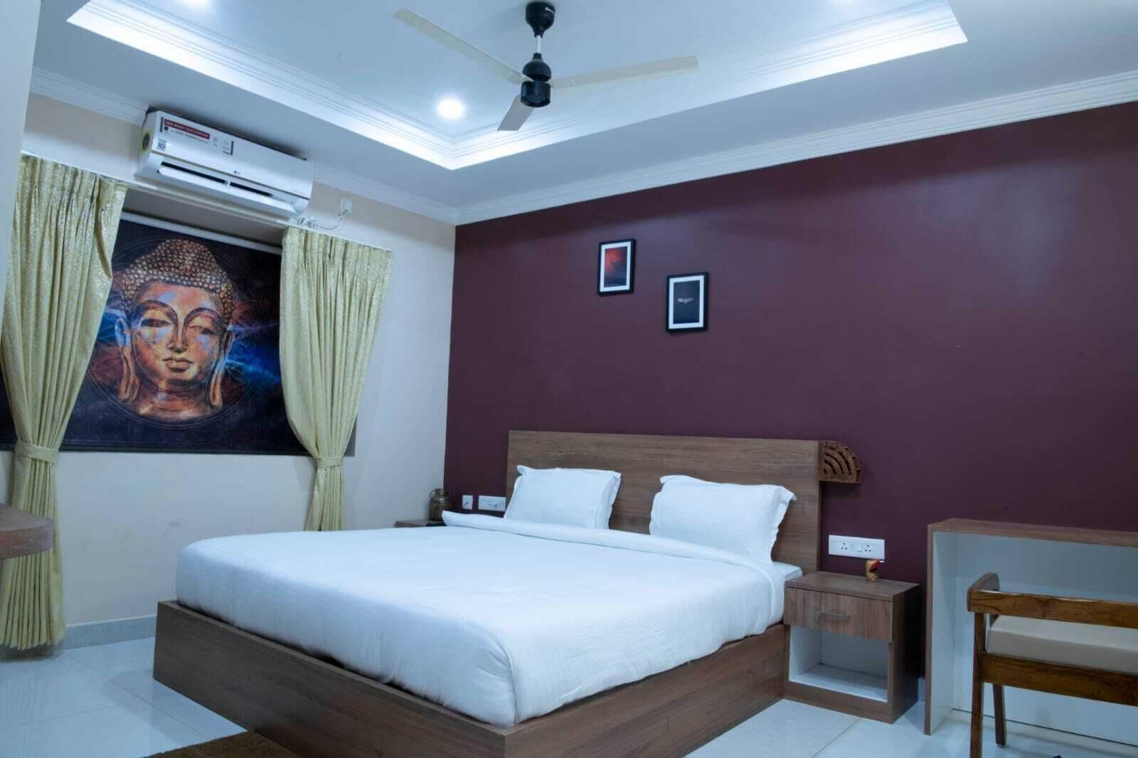 Een slaapkamer met een bed, een plafondventilator, een airconditioning, een nachtkastje, een stoel en een wand met een ingelijst beeld.