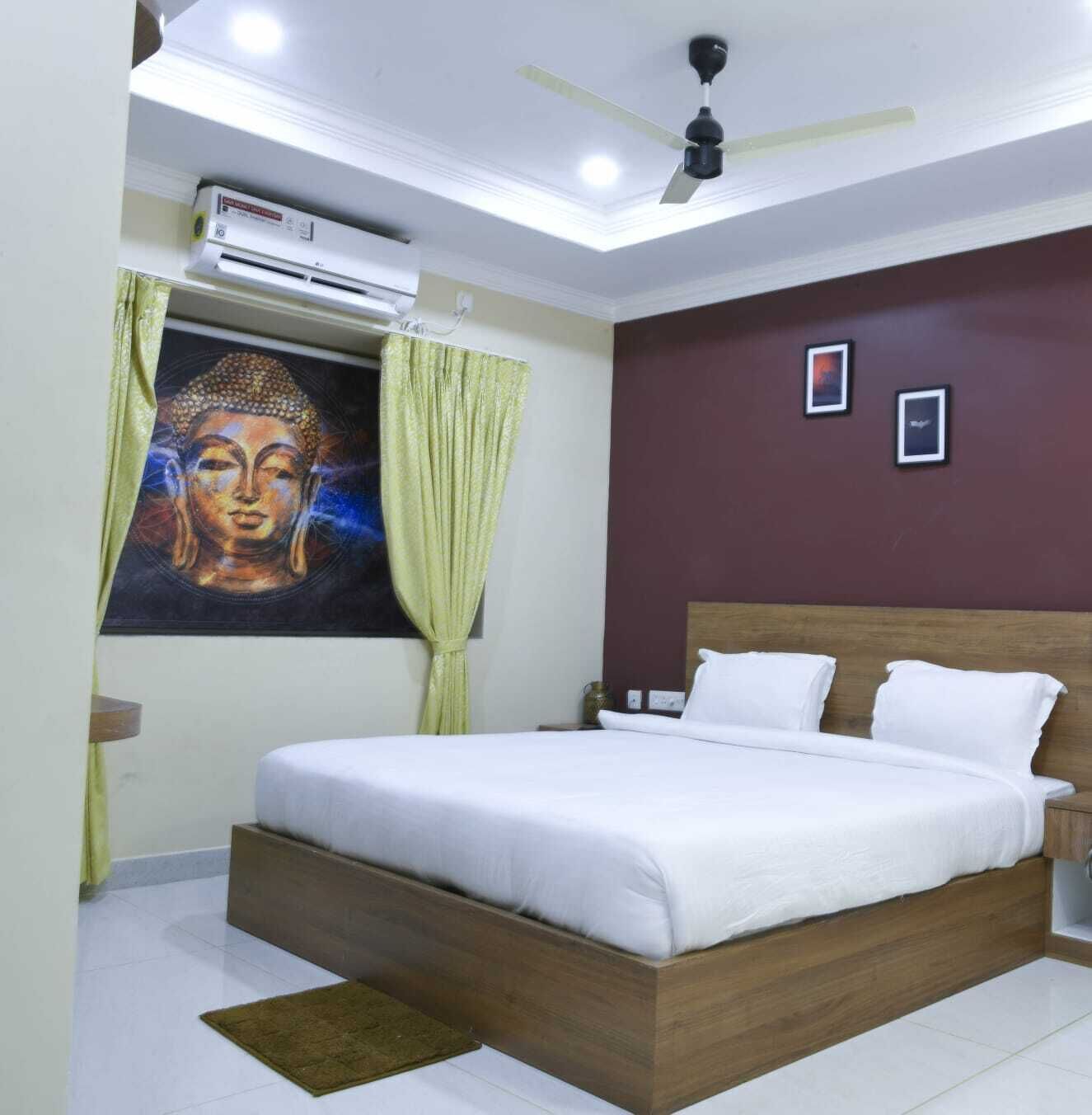 Un dormitorio con cama, ventilador de techo, equipo de aire acondicionado, una pintura de Buda y dos cuadros en la pared.