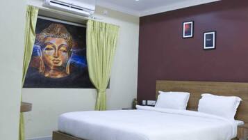Un dormitorio con cama, ventilador de techo, equipo de aire acondicionado, una pintura de Buda y dos cuadros en la pared.