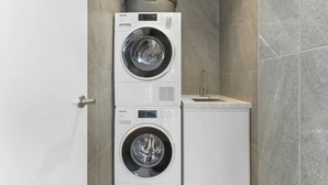 A compact laundry room with two stacked washing machines and a sink. - High-Rise Luxury Stay with Harbour Views – 51 Albert Street (Auckland Central)