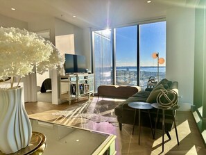A modern living room with a sofa, coffee table, and a large window offering a city view. - High-Rise Luxury Stay with Harbour Views – 51 Albert Street (Auckland Central)