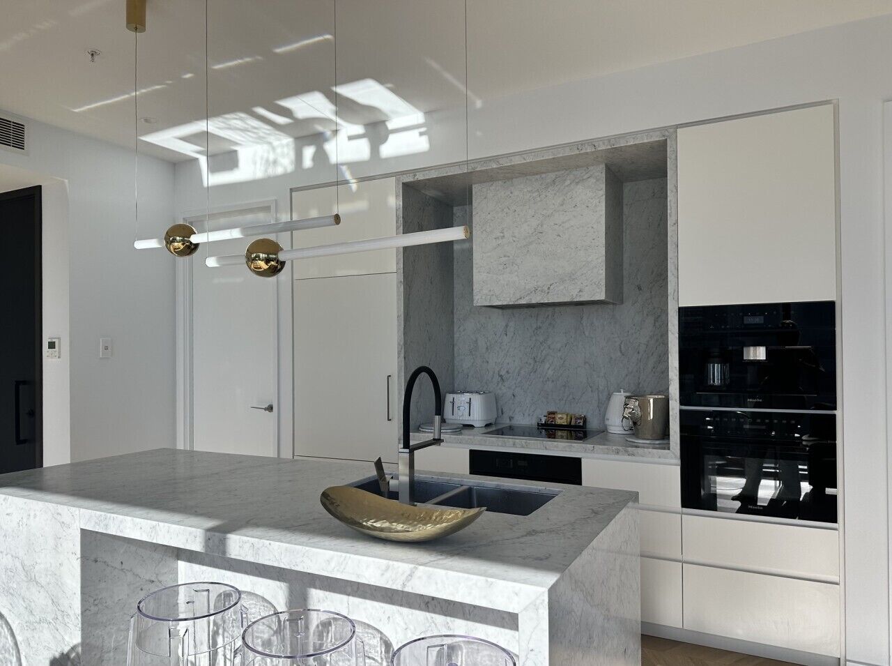 A modern kitchen with a marble countertop, a built-in oven, and a large island with a sink and stools.