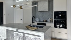 A modern kitchen with a marble countertop, a built-in oven, and a large island with a sink and stools. - High-Rise Luxury Stay with Harbour Views – 51 Albert Street (Auckland Central)