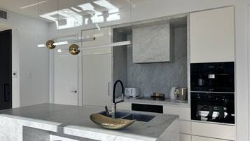 A modern kitchen with a marble countertop, a built-in oven, and a large island with a sink and stools.