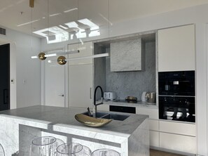 A modern kitchen with a marble countertop, a built-in oven, and a large island with a sink and stools. - High-Rise Luxury Stay with Harbour Views – 51 Albert Street (Auckland Central)