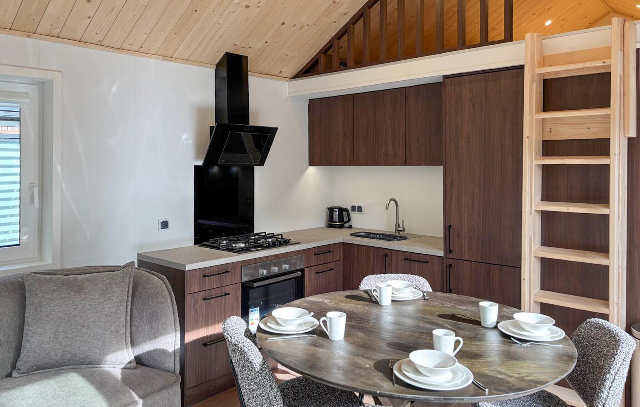 Een moderne keuken met donkerhouten kastjes, een zwart fornuis en een ronde eettafel voor vier personen.