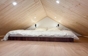 A bedroom with a sloped ceiling, wooden flooring, a bed with white bedding, and two wall-mounted lights. - Stunning home in Oud Gastel with WiFi (Oud Gastel)
