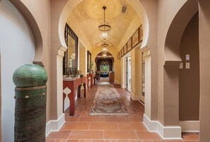 A hallway with a patterned rug, a green decorative column, and a chandelier. - Moroccan Desert Oasis in Serene Neighborhood (Palm Springs)