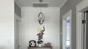 Ein Flur mit weißen Wandverkleidungen, Holzboden, Deckenventilator, einer Kronleuchter und einem dekorativen Schrank sowie einer Tür mit Glasfenster.