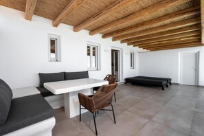 A modern interior with a white bench, wicker chairs, a white table, and a wooden ceiling. - Nero Light-filled Suites (Santorini)