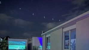 An outdoor pool area with a fire feature, a projection screen, and a dining table. - Beige Beach House Blairgowrie (Blairgowrie)