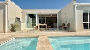 A modern house with a swimming pool, a patio with chairs, and a glass door leading to an interior space. - Beige Beach House Blairgowrie (Blairgowrie)