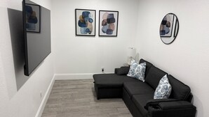 A modern living room with a sectional sofa, a flat-screen TV, abstract wall art, and a round mirror. -     Modern & Cozy Apartment Near Everything You Need! (Valrico)