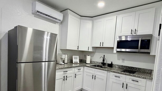 A modern kitchen with white cabinets, a stainless steel refrigerator, a microwave, and a granite countertop. -     Modern & Cozy Apartment Near Everything You Need! (Valrico)