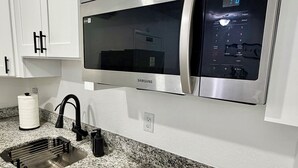 A modern kitchen with white cabinets, a stainless steel microwave, a granite countertop, a black faucet, and a built-in stovetop. -     Modern & Cozy Apartment Near Everything You Need! (Valrico)
