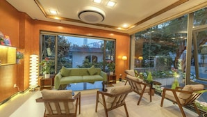 A modern interior with a green sofa, wooden chairs, and a large window offering a view of the outside. - Soluna Dalat Hotel (Xuan Huong - Da Lat)