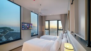 A hotel room with a large window, a bed, a TV mounted on the wall, and a ceiling fan. - Soluna Dalat Hotel (Xuan Huong - Da Lat)