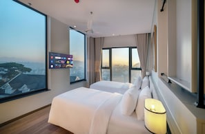 A hotel room with a large window, a bed, a TV mounted on the wall, and a ceiling fan.