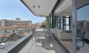 Ein Balkon mit Tisch, Stühlen, einer Couch und einer Glastür zu einem Außenbereich.
