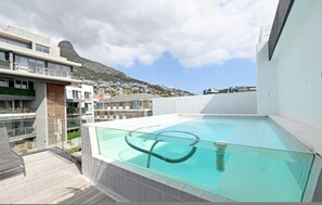 Ein Pool auf dem Dach mit Glasbrüstung, moderne Gebäude und eine gebirgige Kulisse.