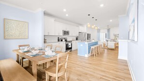 Una cocina moderna con armarios blancos, una isla central y un comedor con muebles de madera.