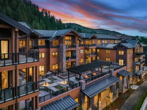 Un hôtel à plusieurs étages doté de balcons, d’espaces extérieurs aménagés pour s’asseoir et offrant une vue sur une colline boisée.